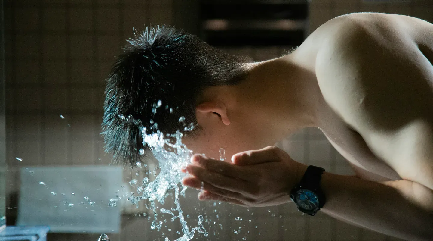 洗面台で水を顔にすくって洗う男性