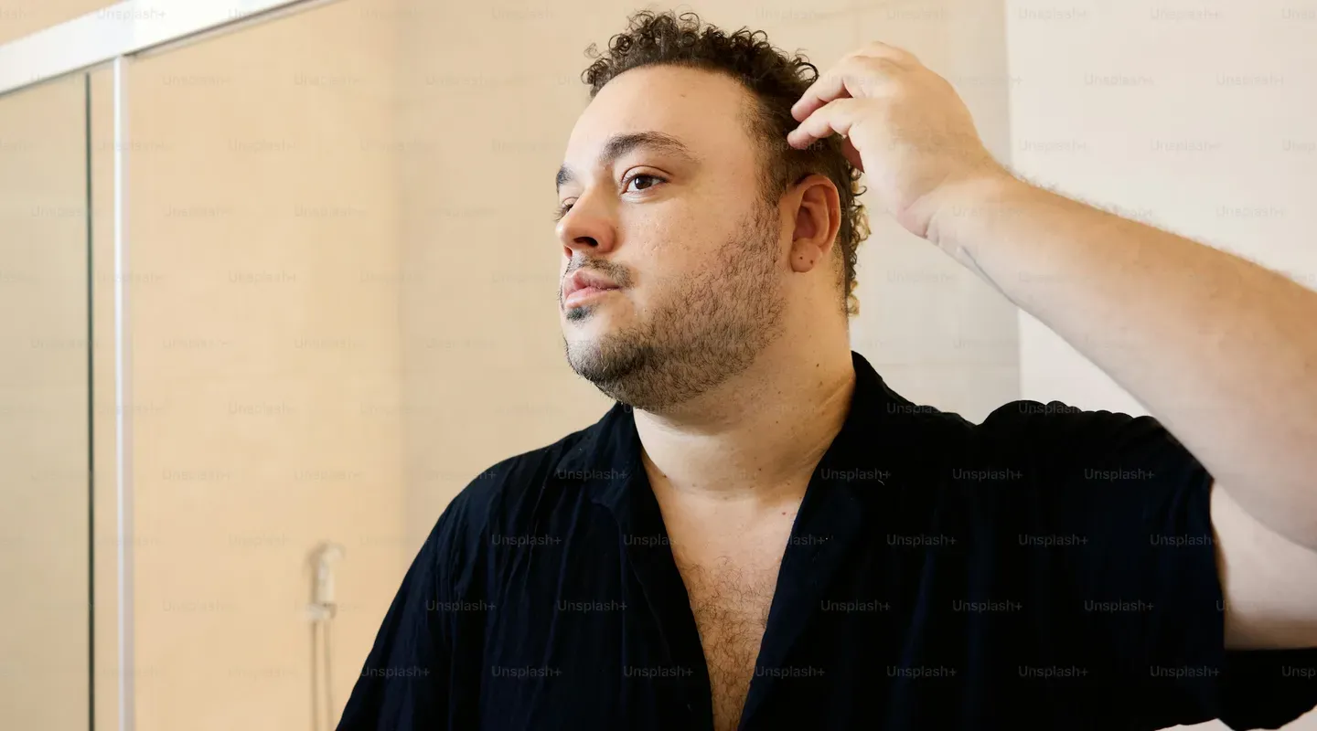 鏡の前に立ち、髪を撫でて状態を確認する男性